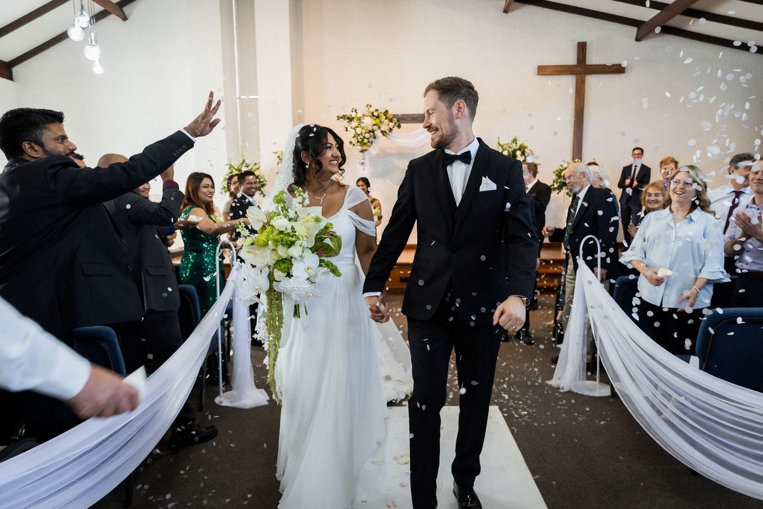 Newlyweds walk down church aisle amid confetti shower with guests celebrating their wedding.