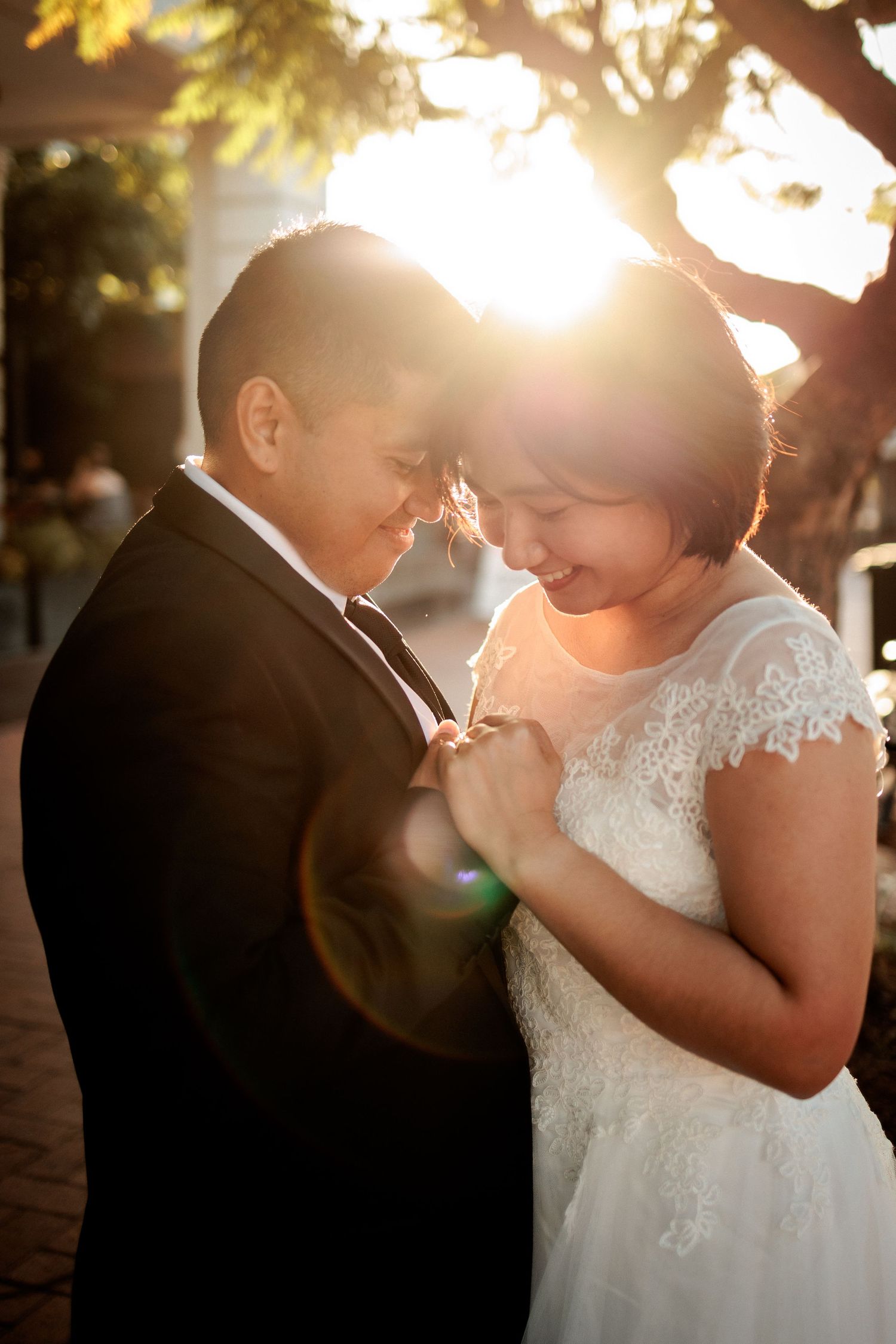 Bride and groom share a tender moment with foreheads touching, bathed in golden sunlight during outdoor wedding photos.
