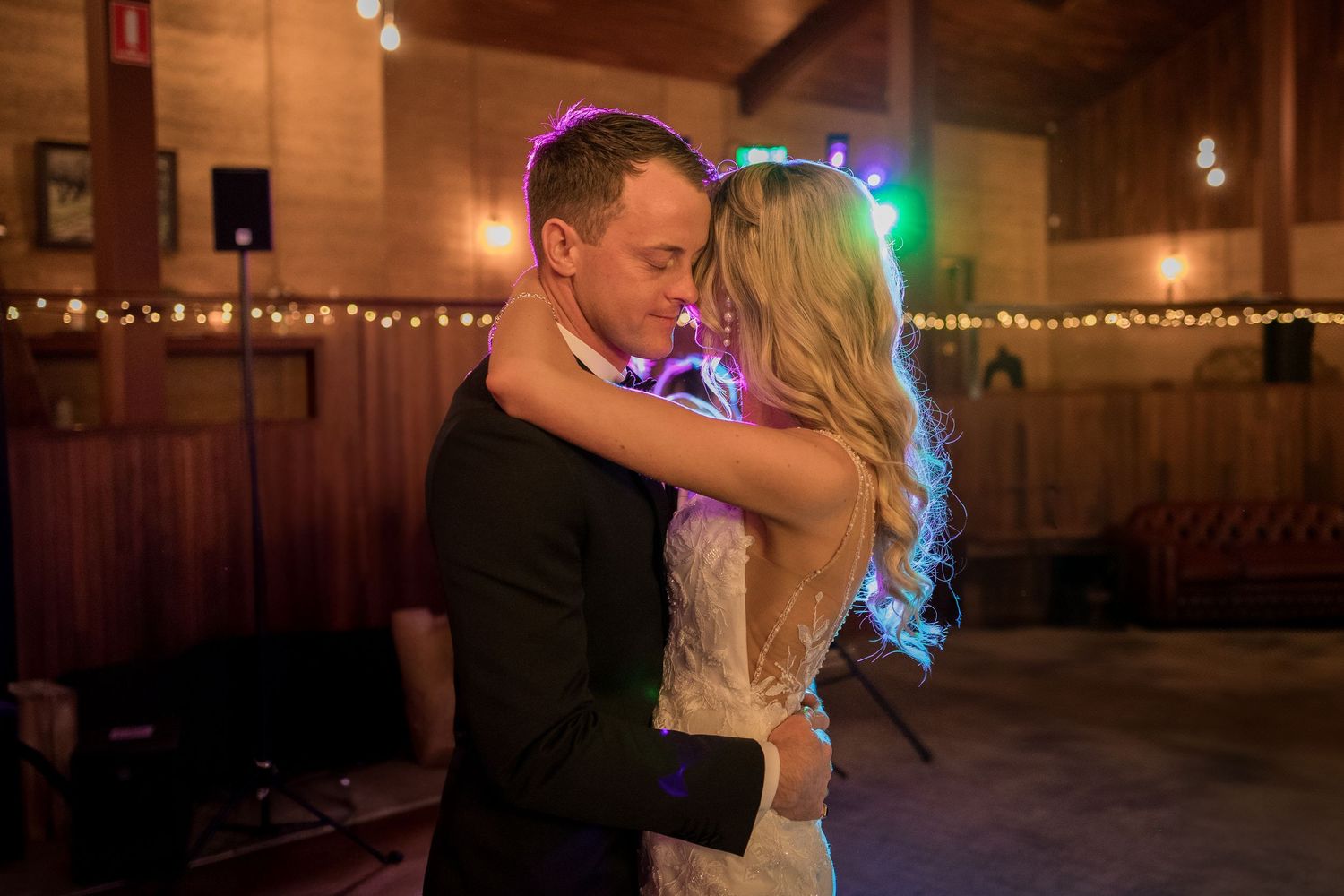 First dance moment in rustic venue with colorful lighting effects.