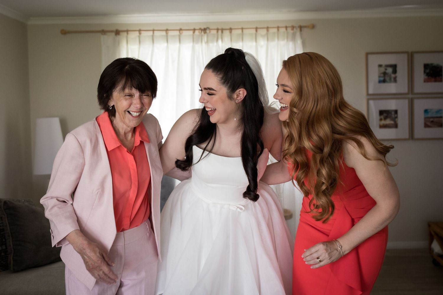 Bridal party in pink and coral dresses laughing together during pre-wedding preparations.