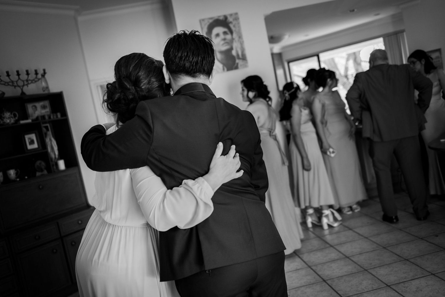 Black and white photo of wedding guests embracing at indoor reception.
