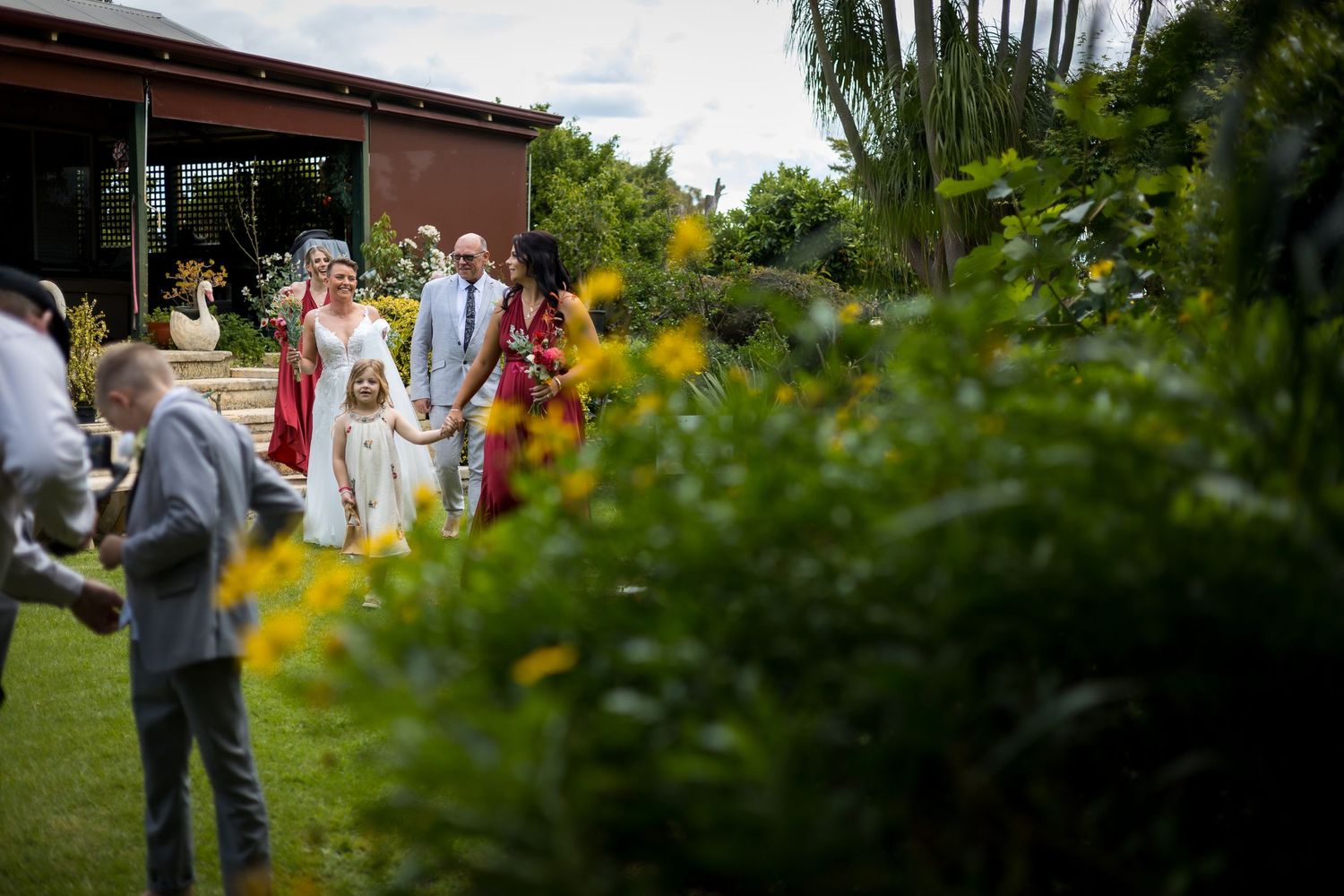 Wedding guests gather outdoors under lush greenery during a garden ceremony celebration.