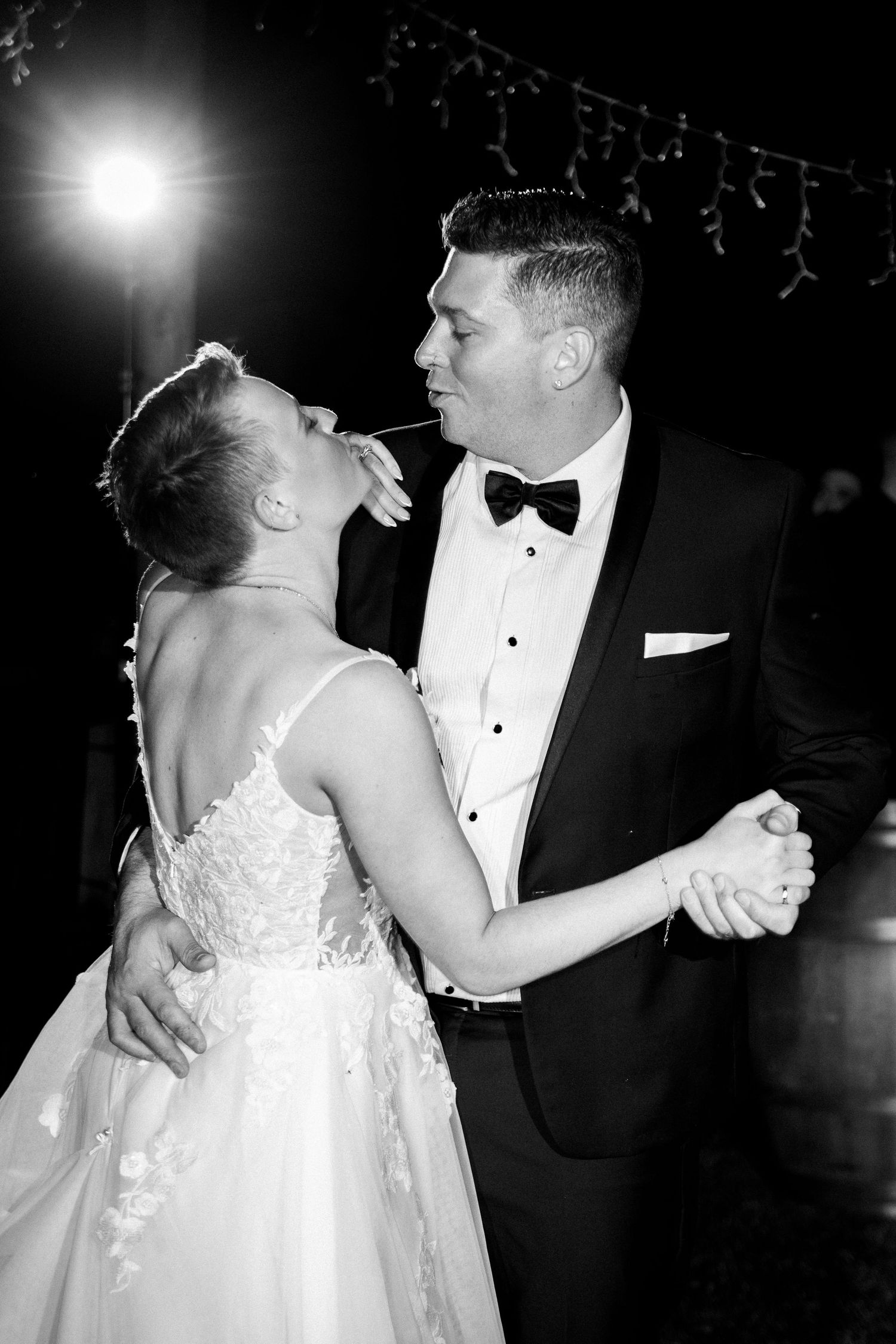 Black and white photo of a bride and groom sharing their first dance at a wedding reception under soft lighting.