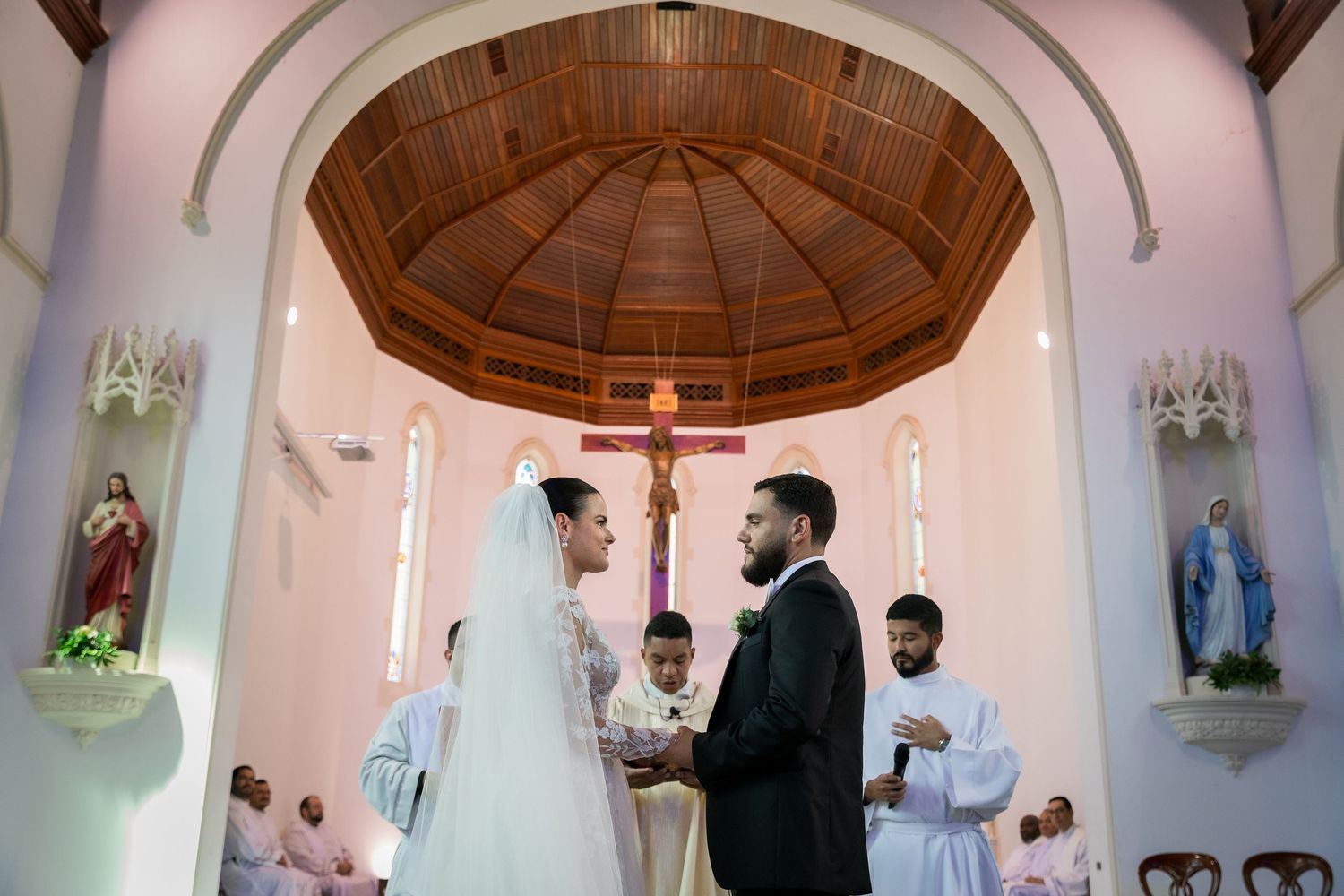 Couple exchanging vows at a Catholic church wedding ceremony with a crucifix altar and stained glass windows.