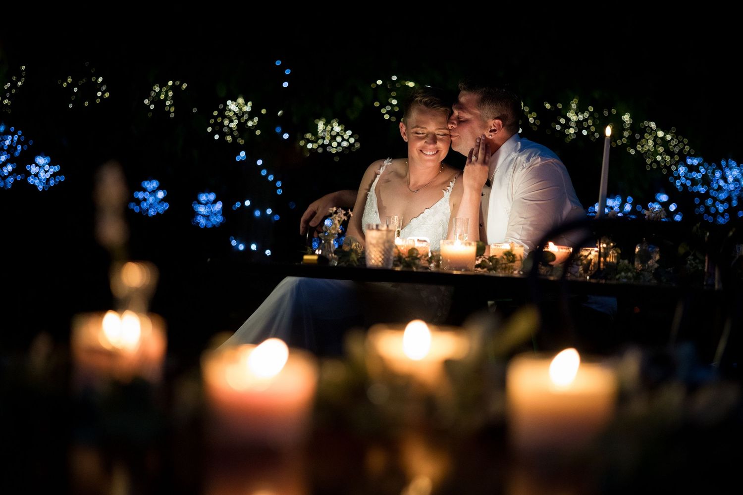 Candlelit table settings create an intimate atmosphere at an outdoor evening wedding reception.