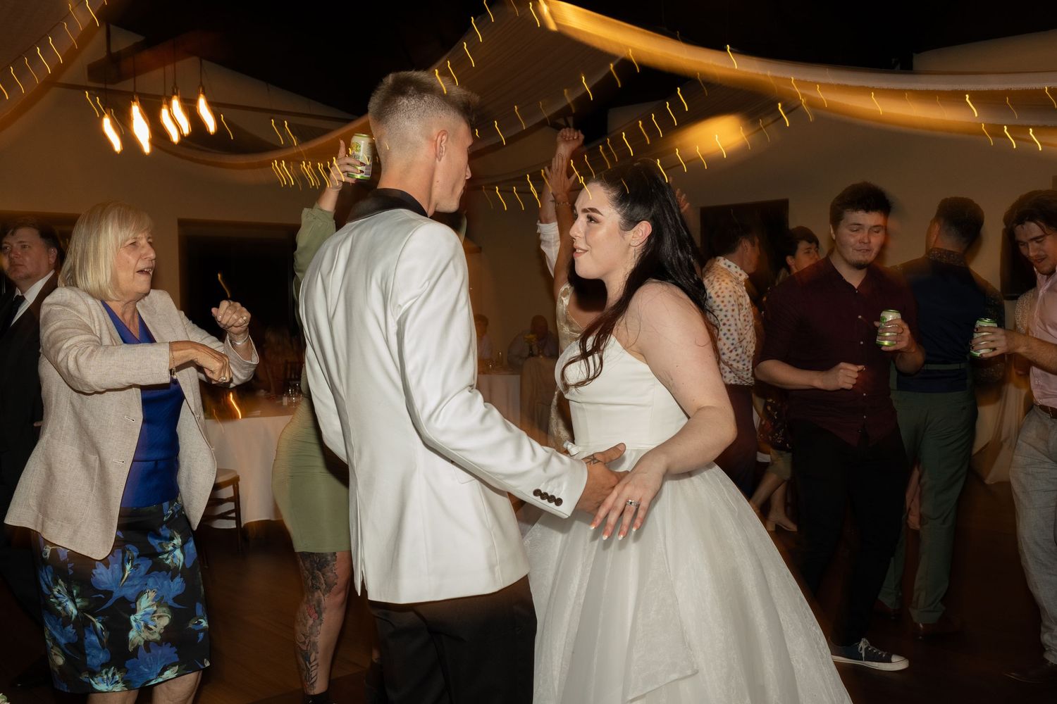 Dancing couples enjoying the reception with decorative lighting overhead.