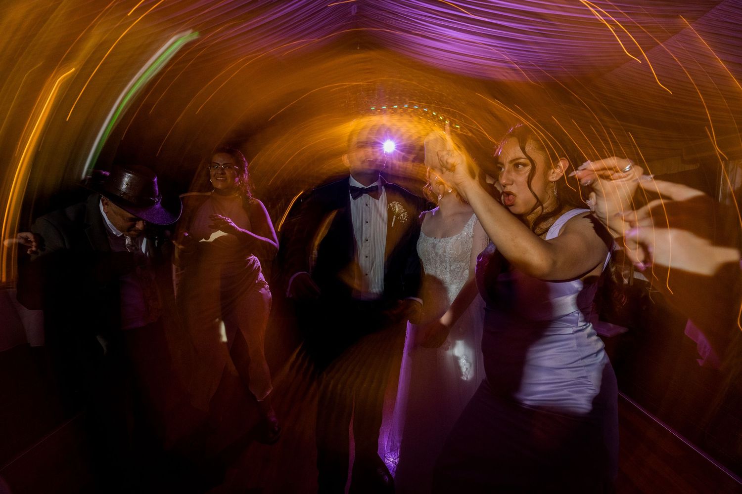 Motion-blurred photo of wedding party dancing under colorful lights.