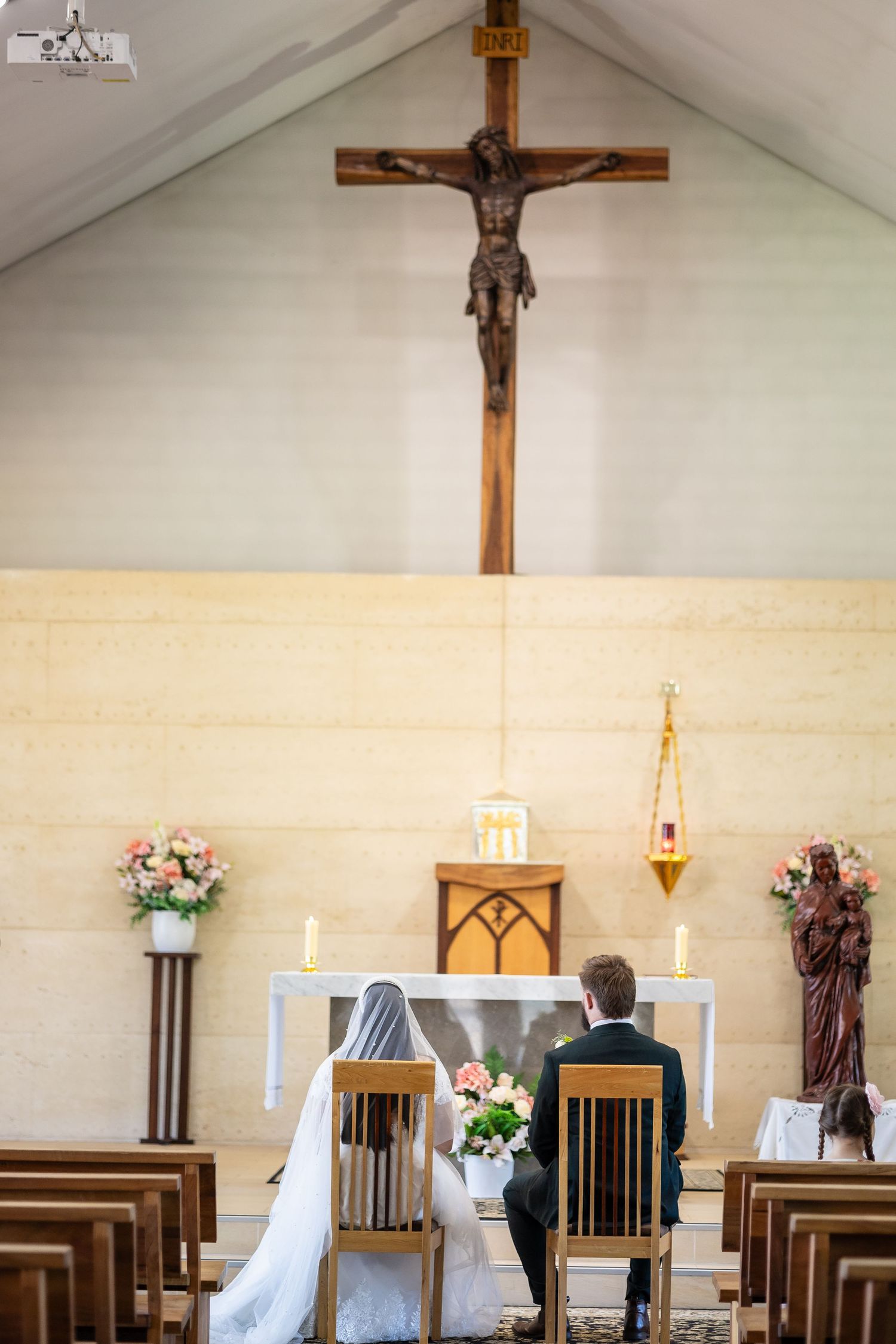 Bride and groom kneeling at church altar during Catholic wedding ceremony with crucifix above.