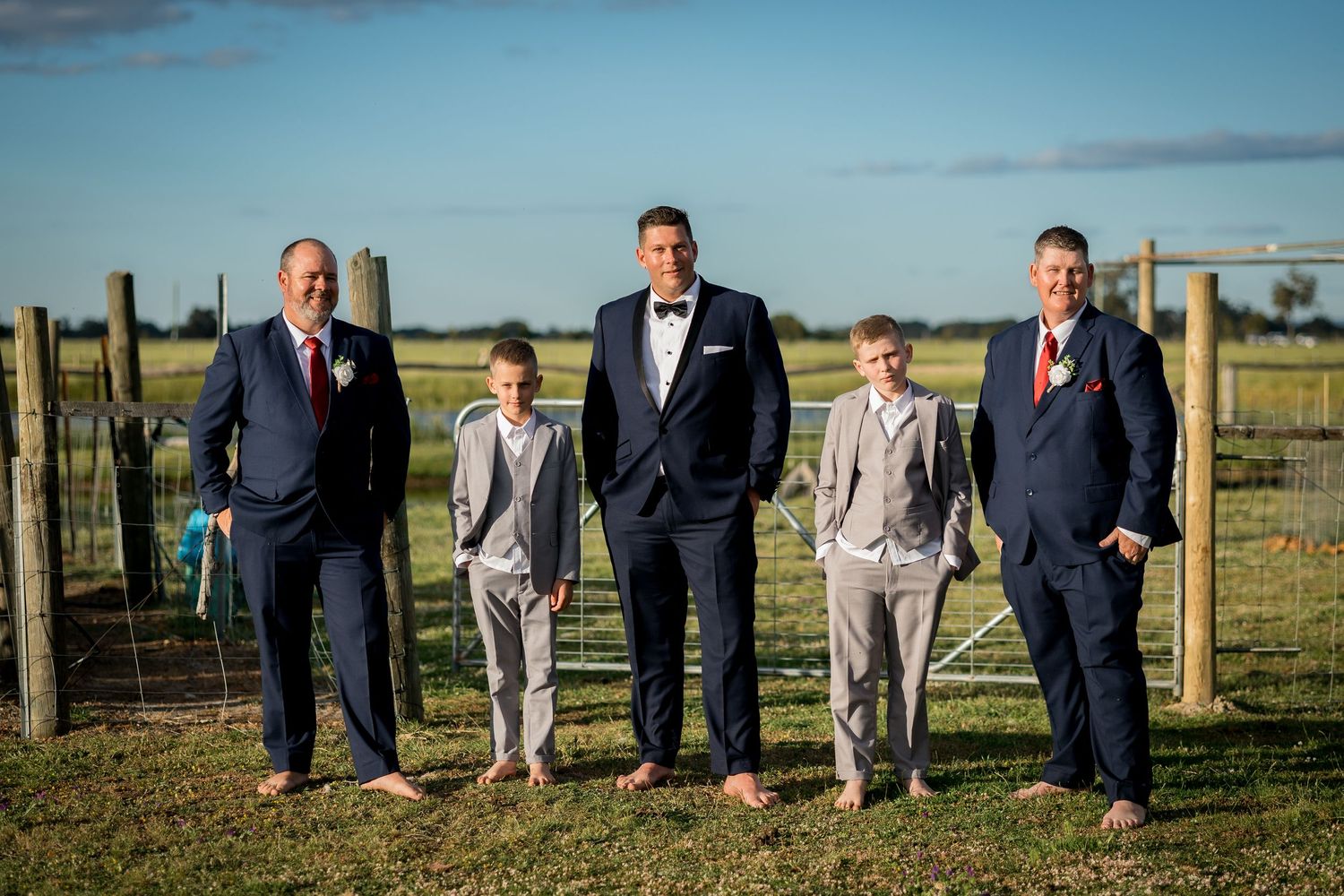 Groomsmen in navy suits and gray pants pose casually in outdoor field setting.