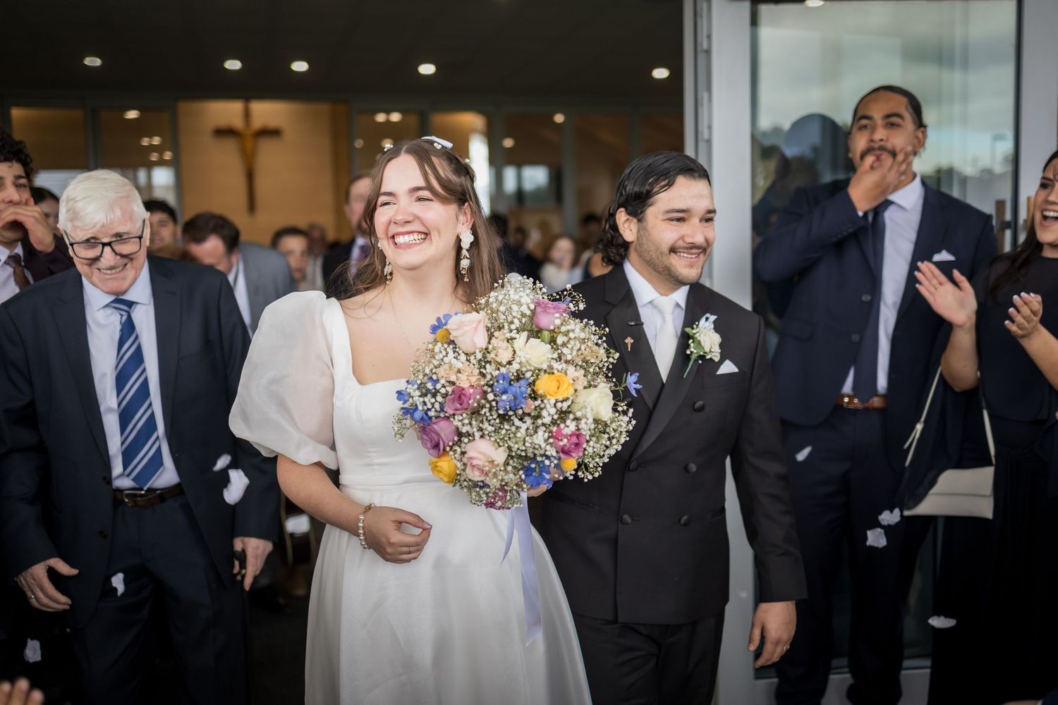 Smiling bride in white dress holding colorful bouquet walks with groom in suit after wedding ceremony.