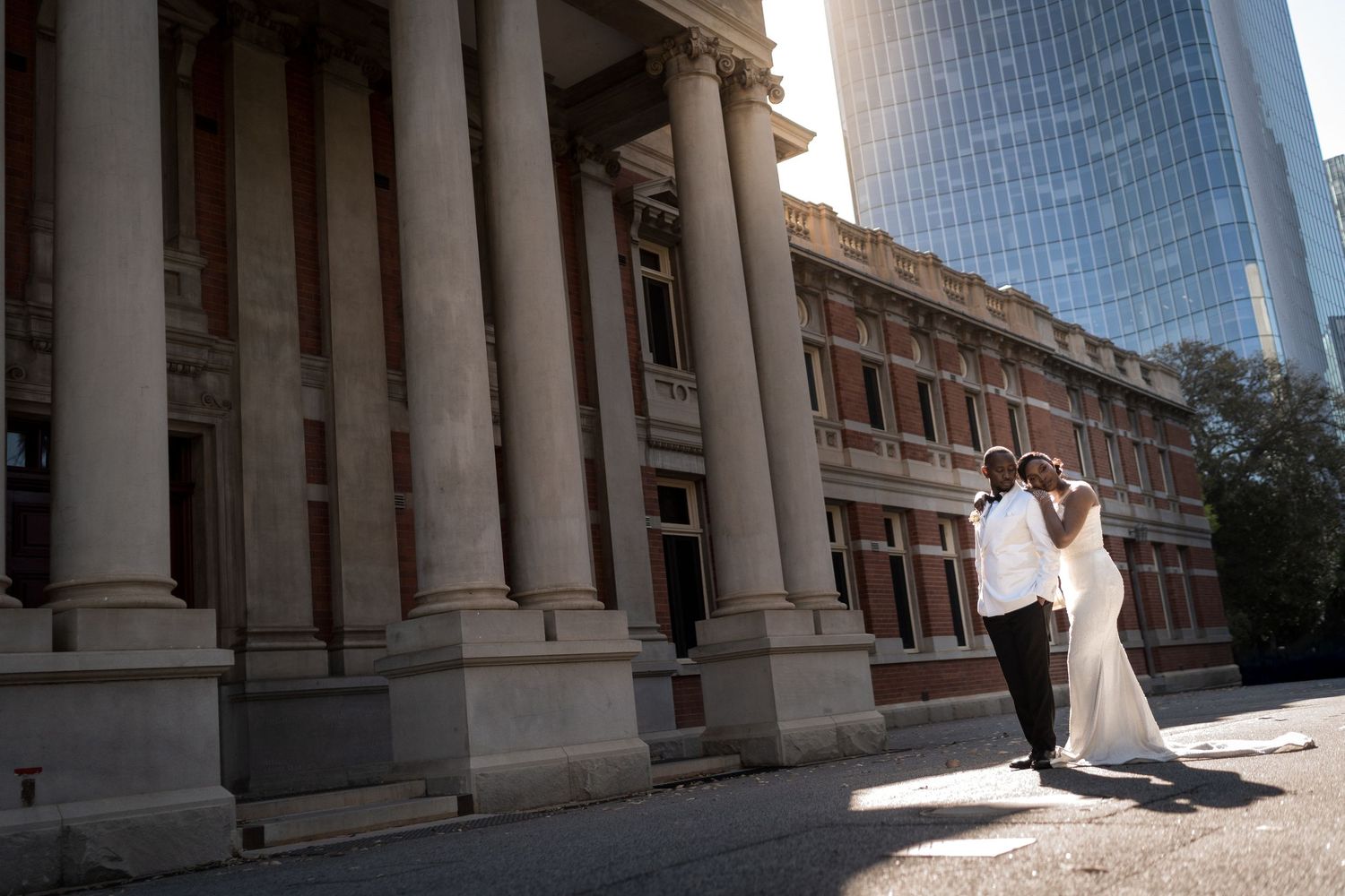 Elegant bride and groom pose in front of a grand historic building with towering columns in the city.