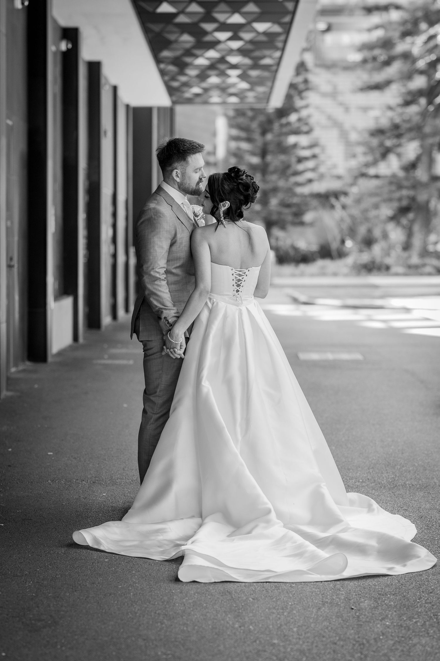 Bride and groom hold hands walking in elegant wedding attire, black and white portrait.