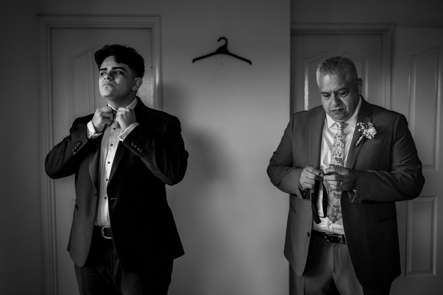 Two men in suits adjust their ties in black and white photo.