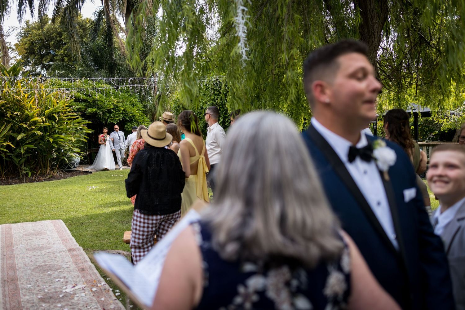 Elegant outdoor wedding ceremony under drooping willow trees on a sunny afternoon.