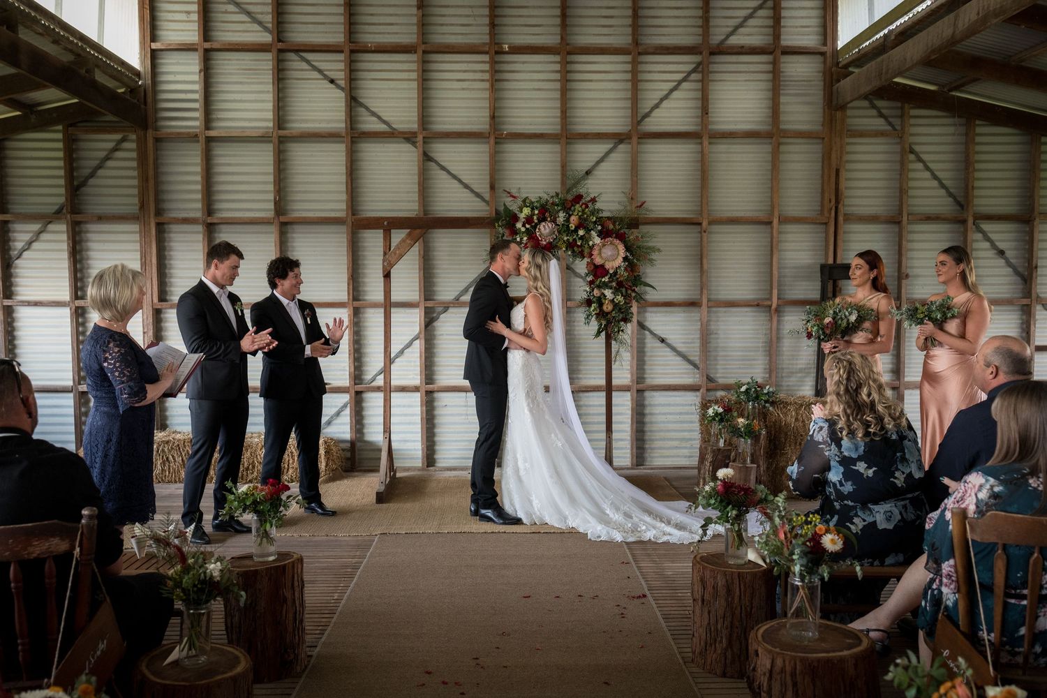Wide angle view of a barn wedding ceremony with guests seated on both sides of the aisle.