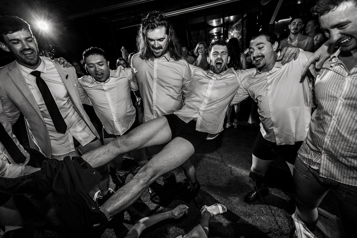 Black and white photo of groomsmen celebrating energetically on the dance floor at wedding reception.
