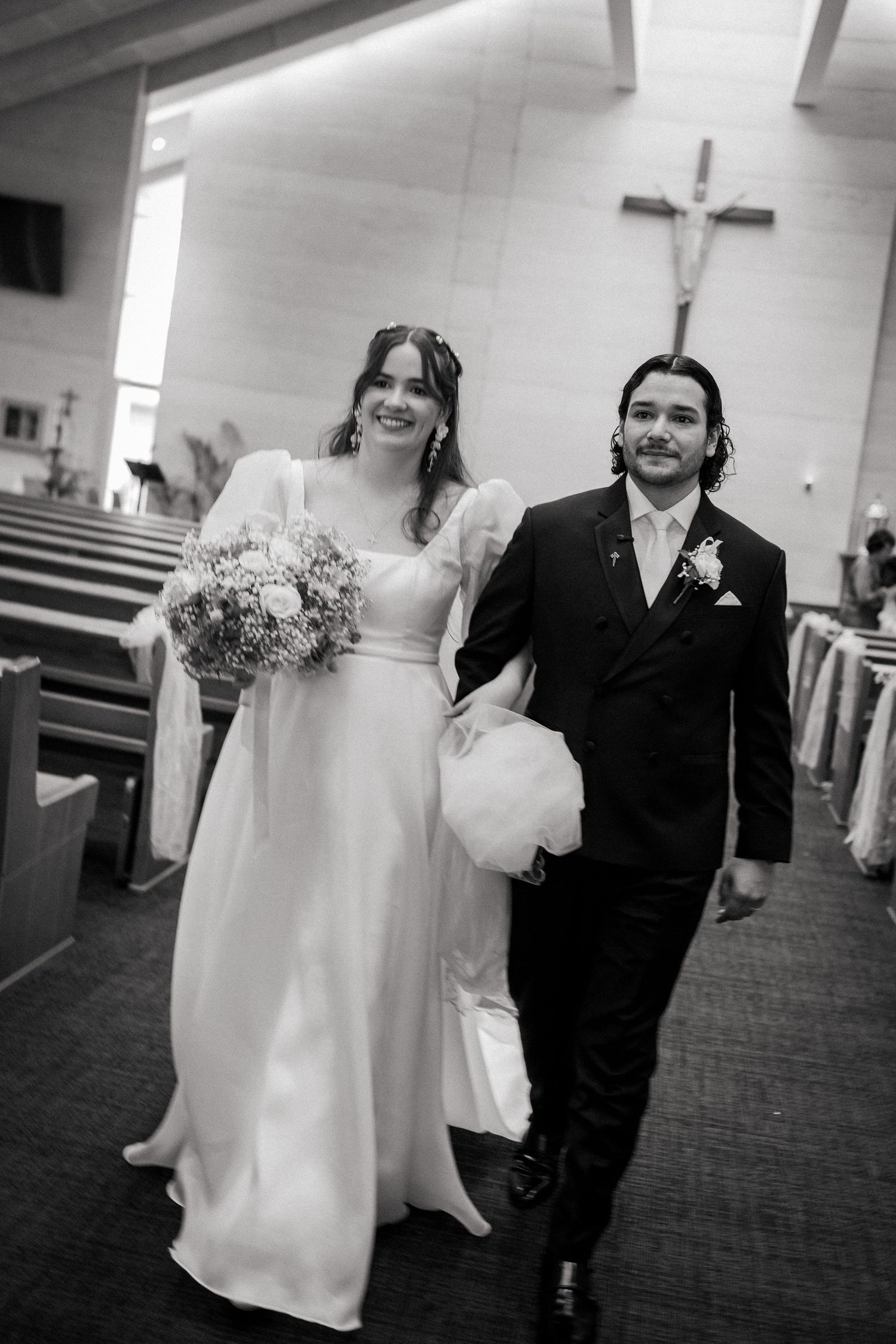 Black and white photo of a smiling bride and groom walking down the church aisle after their wedding ceremony.