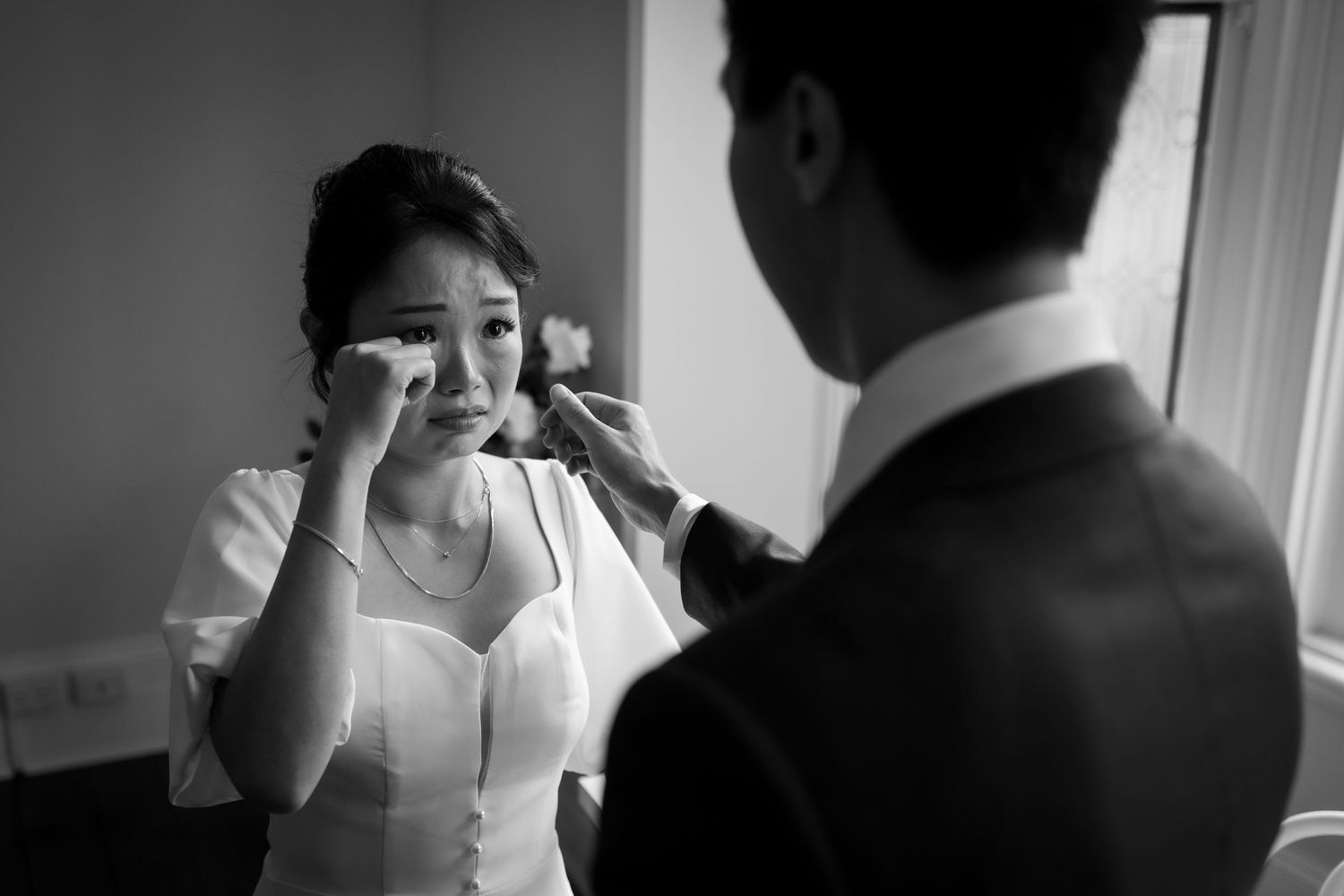 Black and white photo of a bride wiping tears while groom gently touches her face on their wedding day.