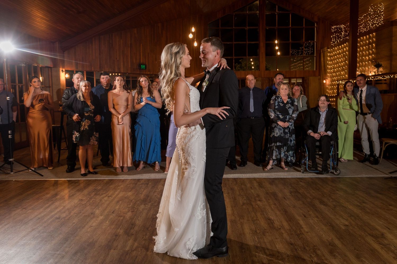 Wedding celebration on wooden dance floor with guests watching.