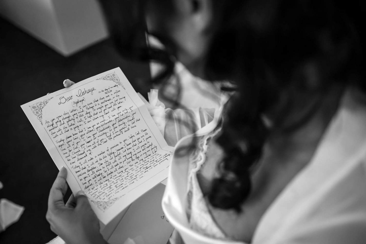 Black and white photo of a bride reading a handwritten letter, holding it with both hands on her wedding day.