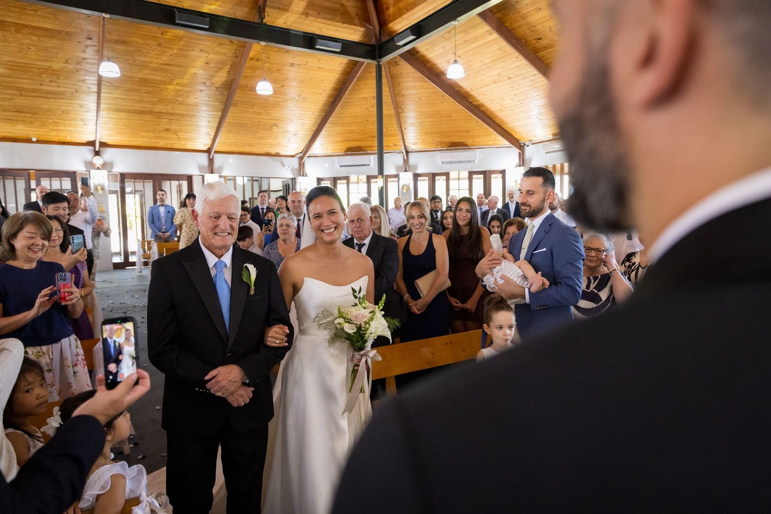 Bride walks down the aisle with her father during an elegant indoor wedding ceremony.