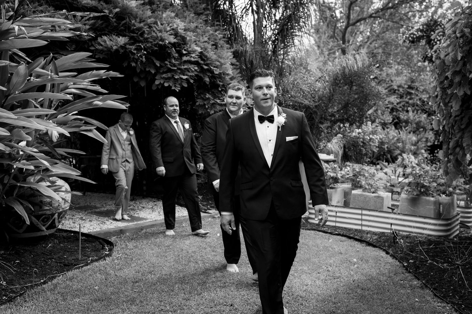 Wedding party members walking through a lush garden pathway.