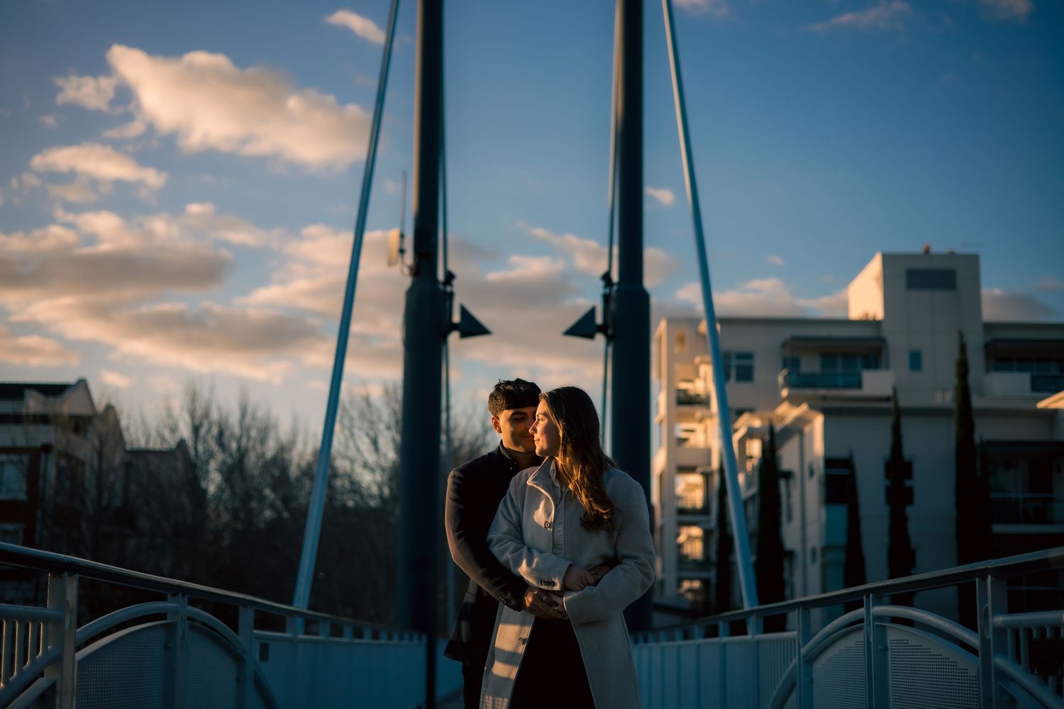 A couple embraces against a dramatic sunset cityscape with silhouetted buildings and warm clouds.