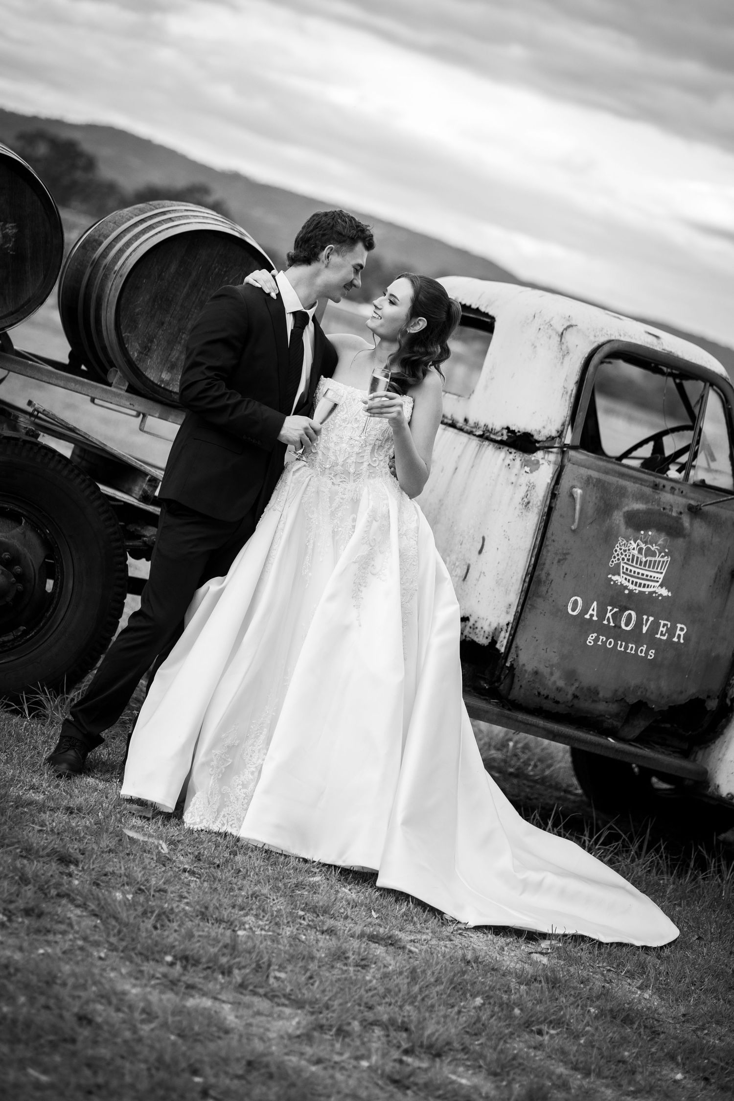 Bride and groom share a romantic moment beside a vintage Oakover Grounds truck in black and white.