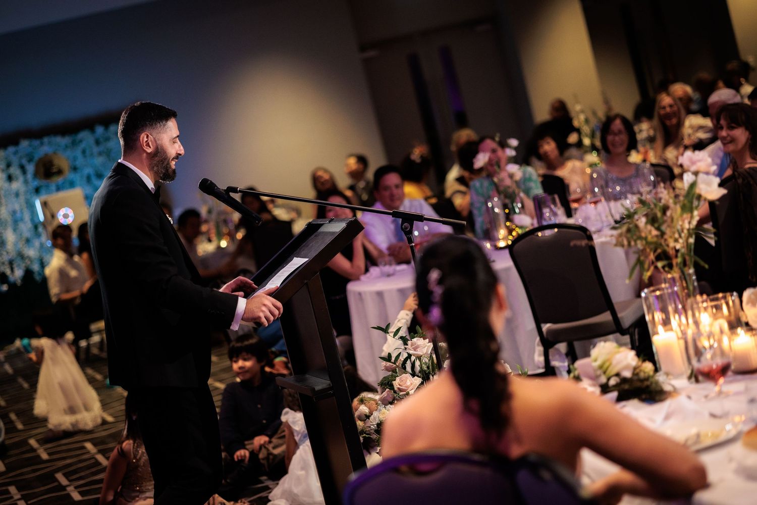 Groom delivers a heartfelt speech at a podium during an elegant candlelit wedding reception.