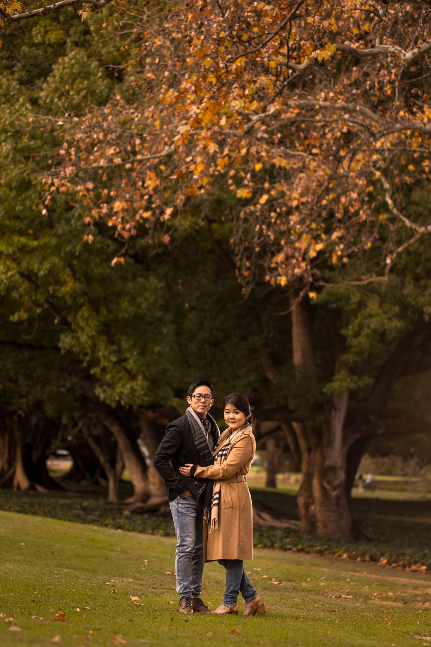 Couple embracing in a park surrounded by autumn trees with golden foliage.