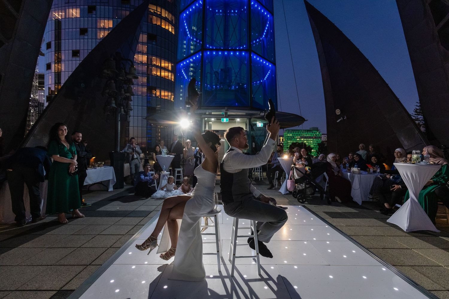 Bride and groom share first dance on illuminated white floor at elegant outdoor rooftop wedding reception at night.