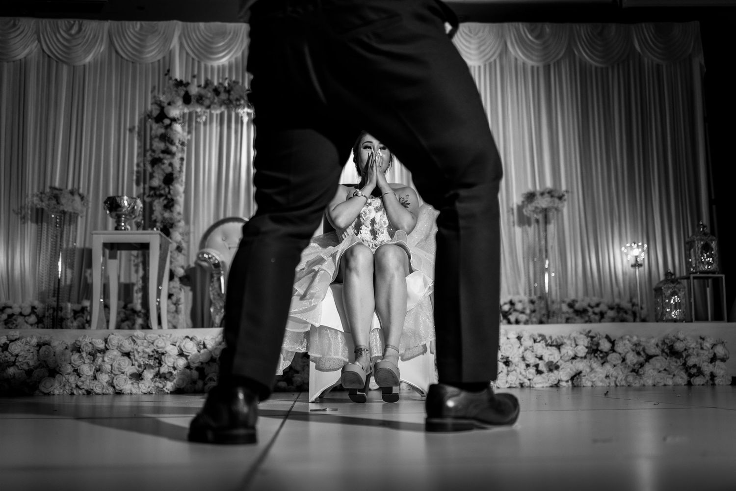 Black and white wedding photo of bride seated while groom stands close during elegant reception ceremony.
