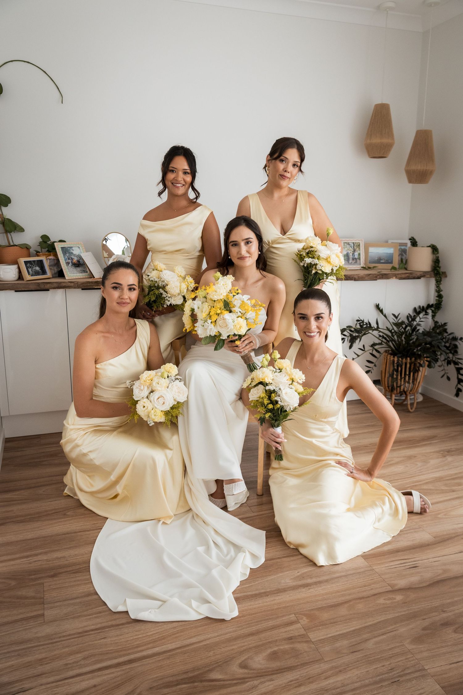 Bride in white gown with four bridesmaids in yellow satin dresses holding bouquets of white and yellow flowers.