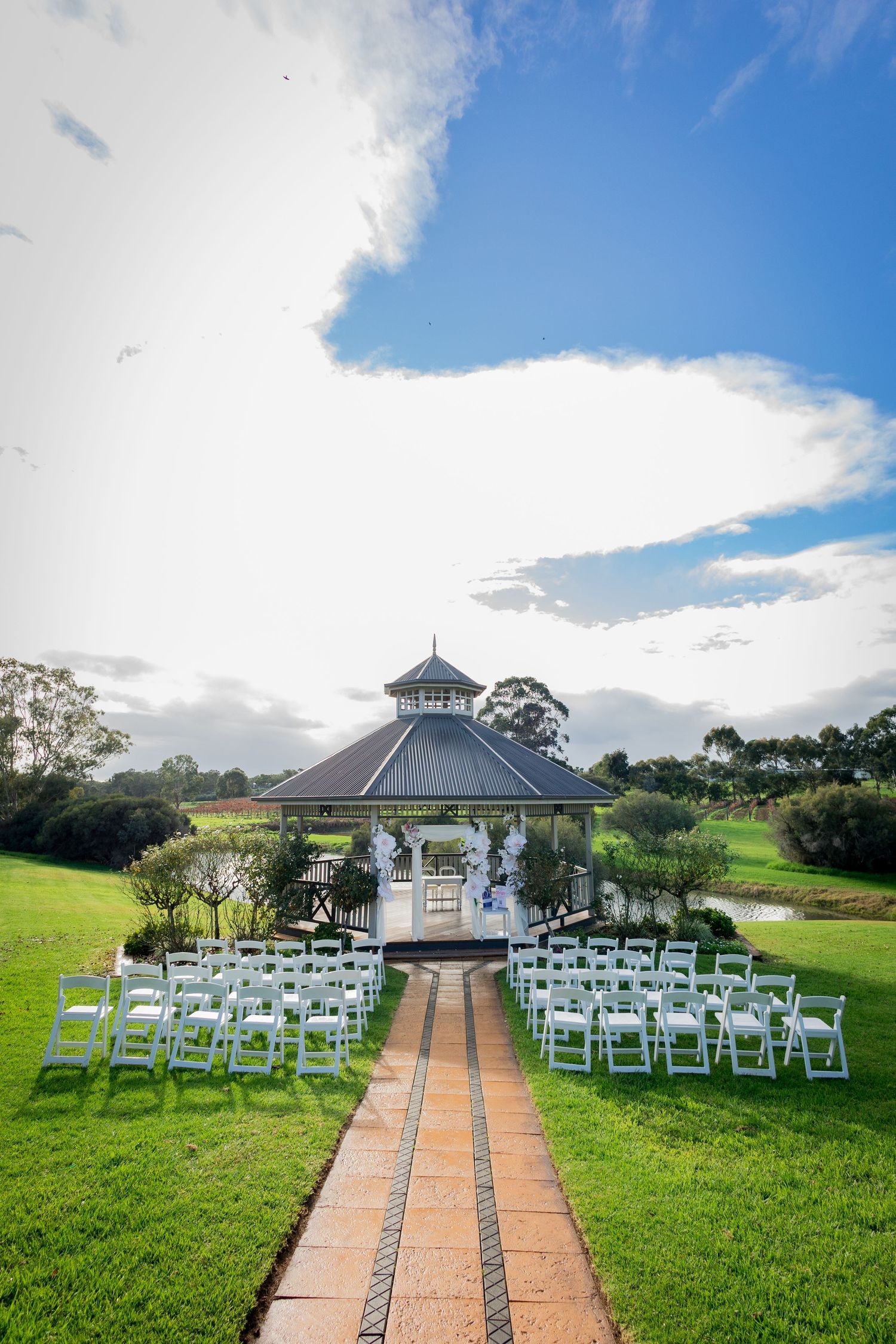 White chairs line a garden path leading to an elegant gazebo for an outdoor wedding ceremony.