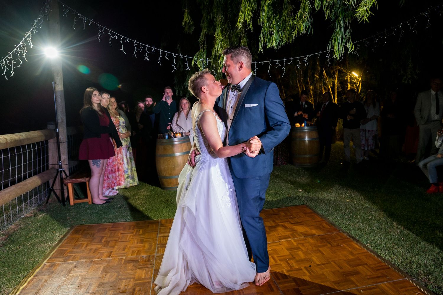 Couples dance together on an outdoor wooden dance floor under string lights at a wedding reception.
