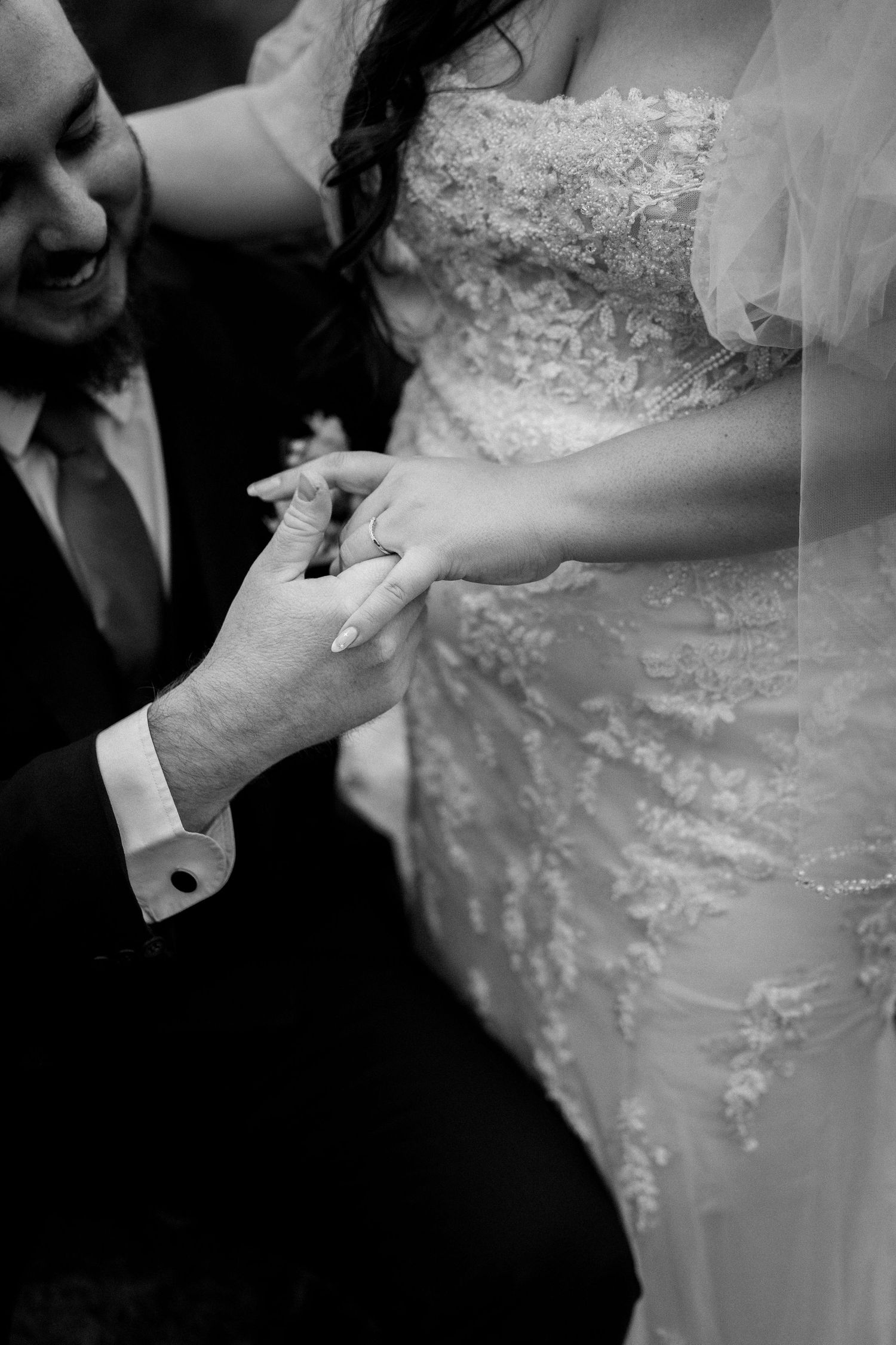 Black and white photo of groom placing wedding ring on bride's finger during ceremony.