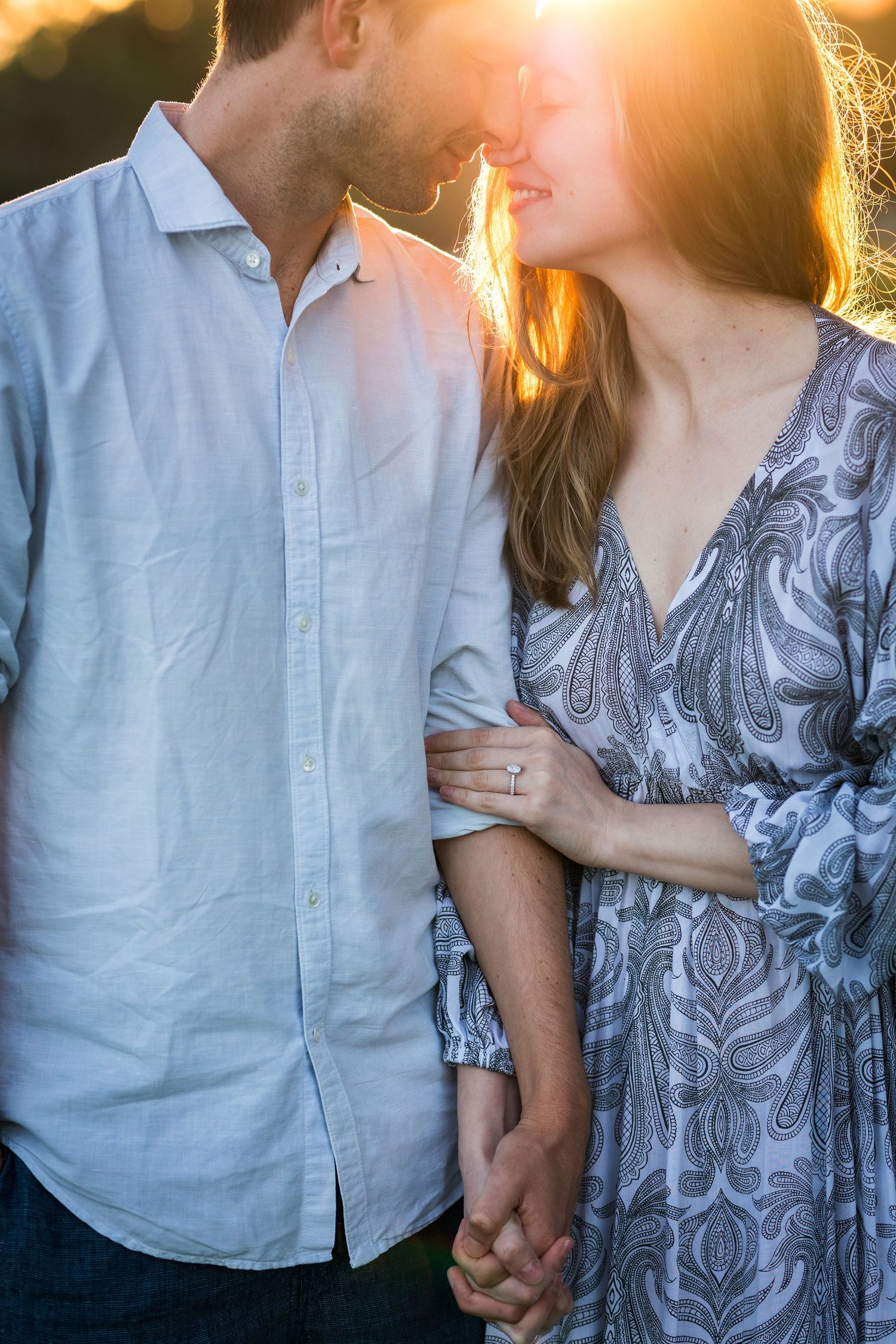 Engaged couple holding hands and smiling at sunset showing engagement ring.