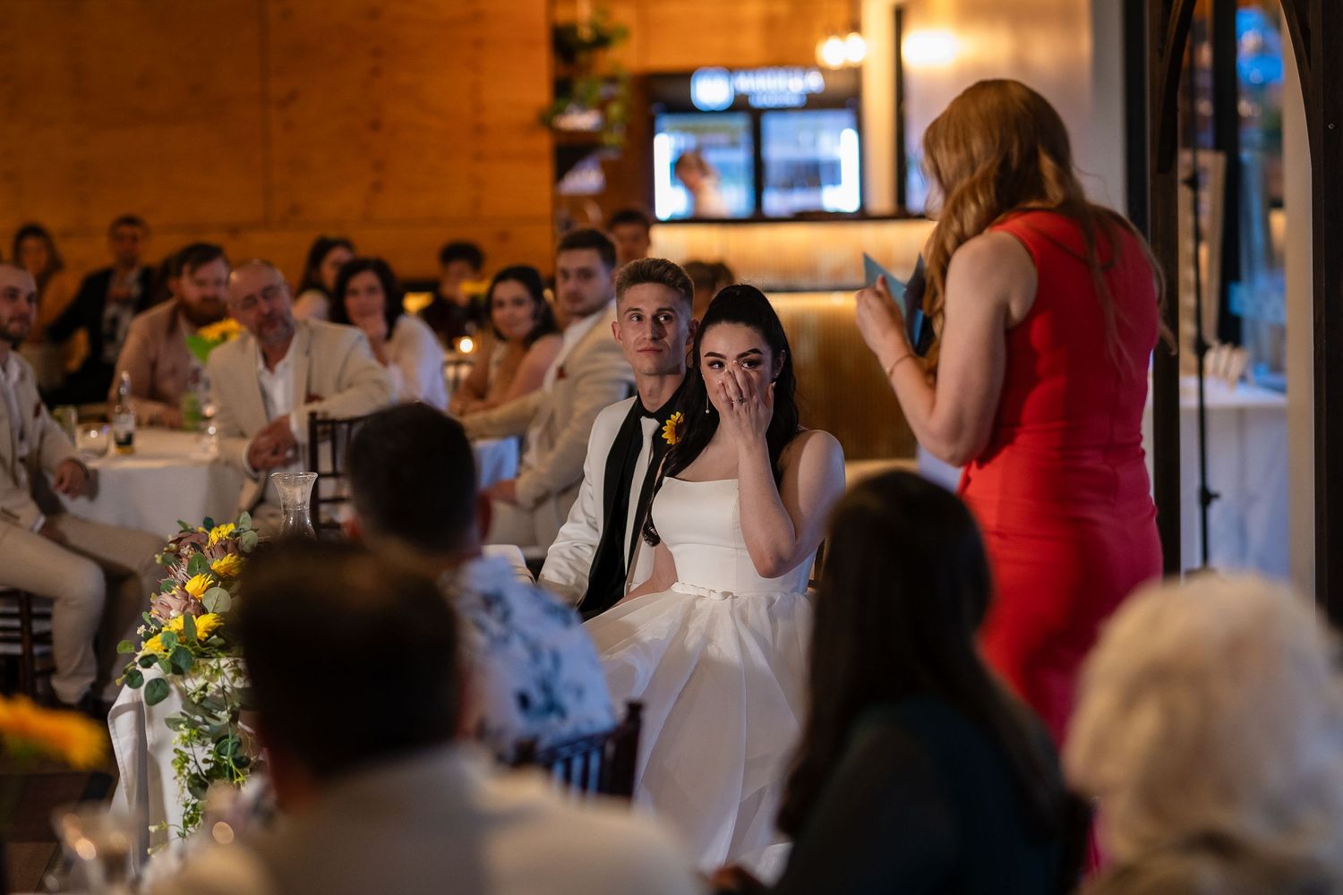 Wedding reception guests celebrate in warm indoor lighting at venue.
