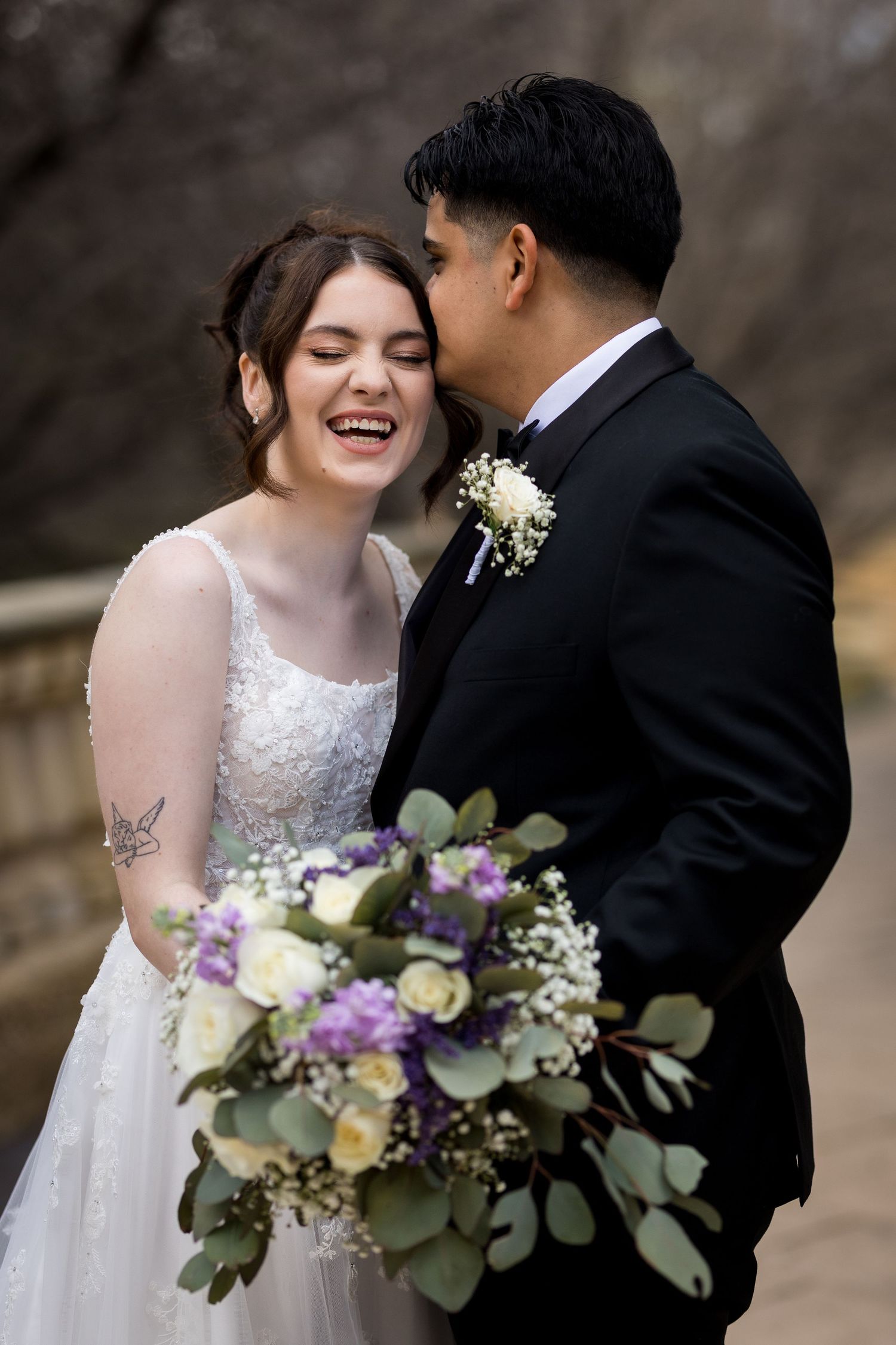 Romantic wedding couple shares intimate moments while holding a purple and white floral bouquet.