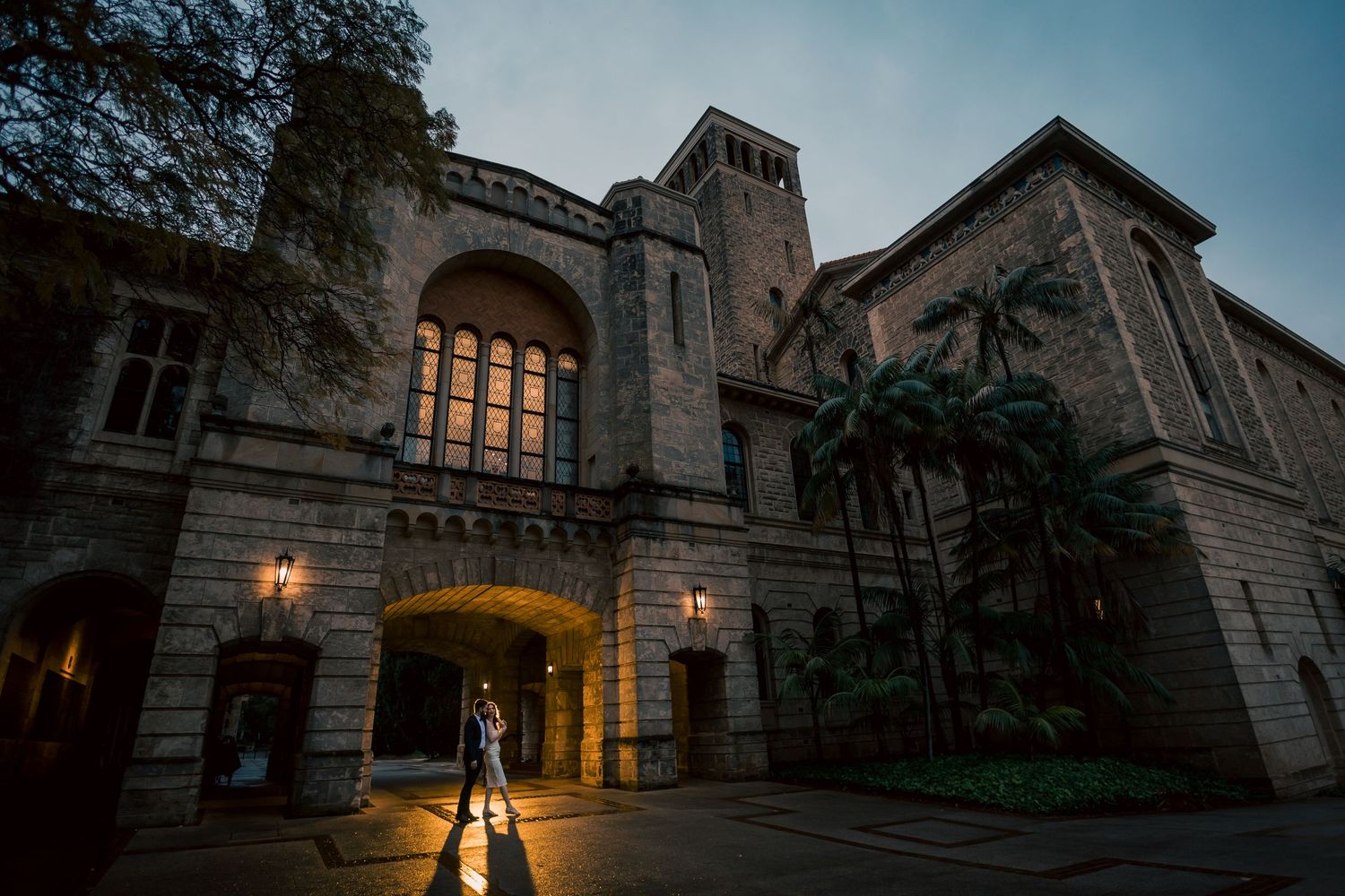Gothic stone building illuminated at dusk with warm lighting in the windows.