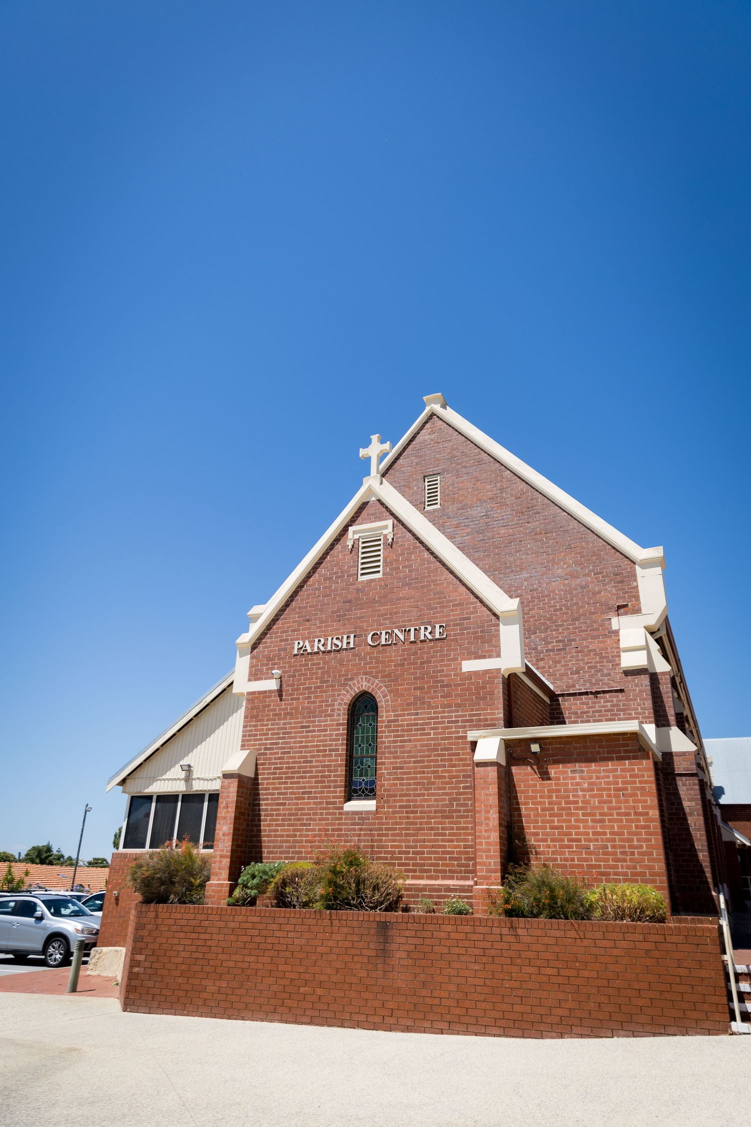 Brick Parish Centre building with white trim and cross on rooftop under clear blue sky.