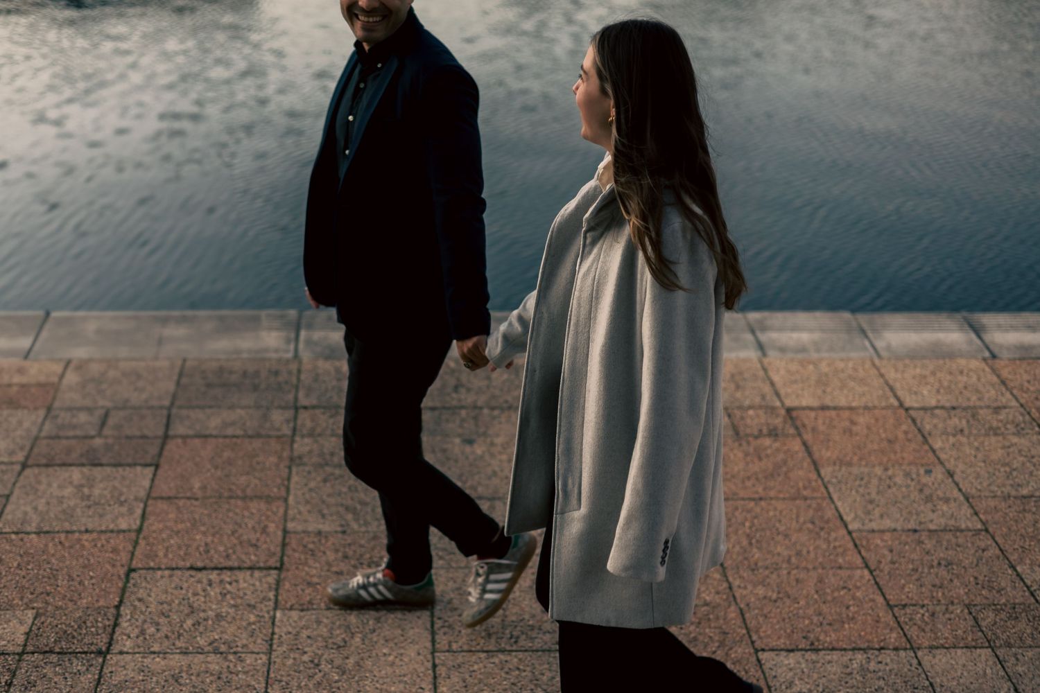 Two figures in silhouette stand together on a tiled walkway at dusk.