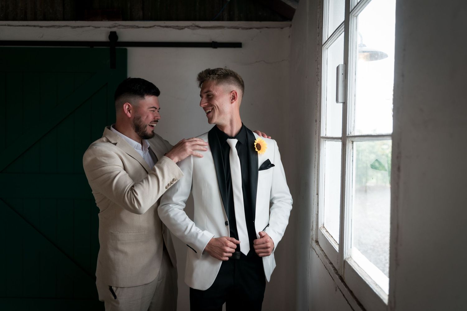 Groomsmen in light suits share candid moments by large windows.