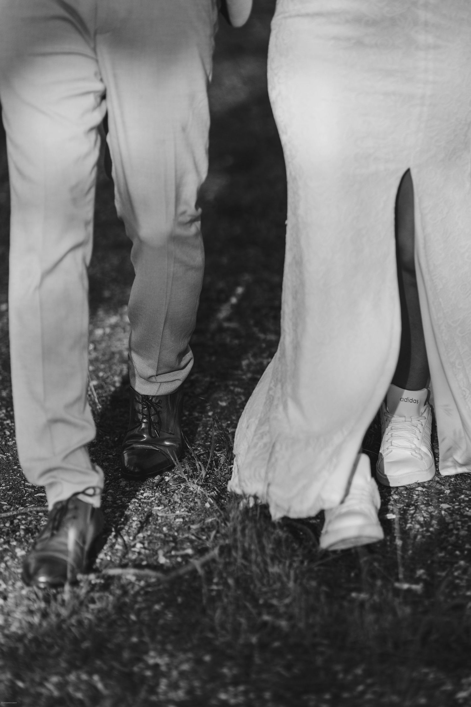 Black and white close-up of bride in sneakers and groom in dress shoes walking.