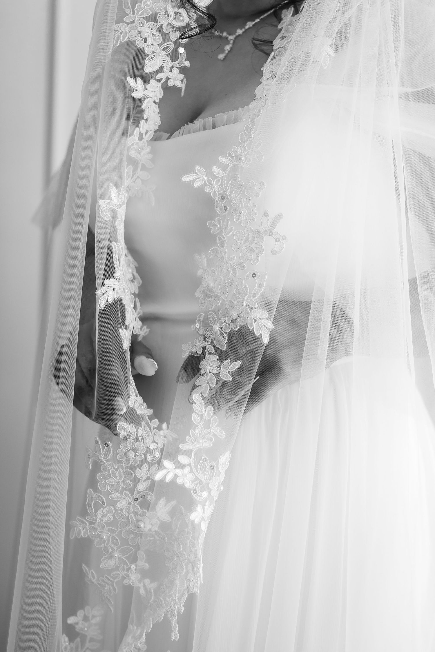 Black and white close-up of bride in lace wedding veil with delicate floral embroidery detail.