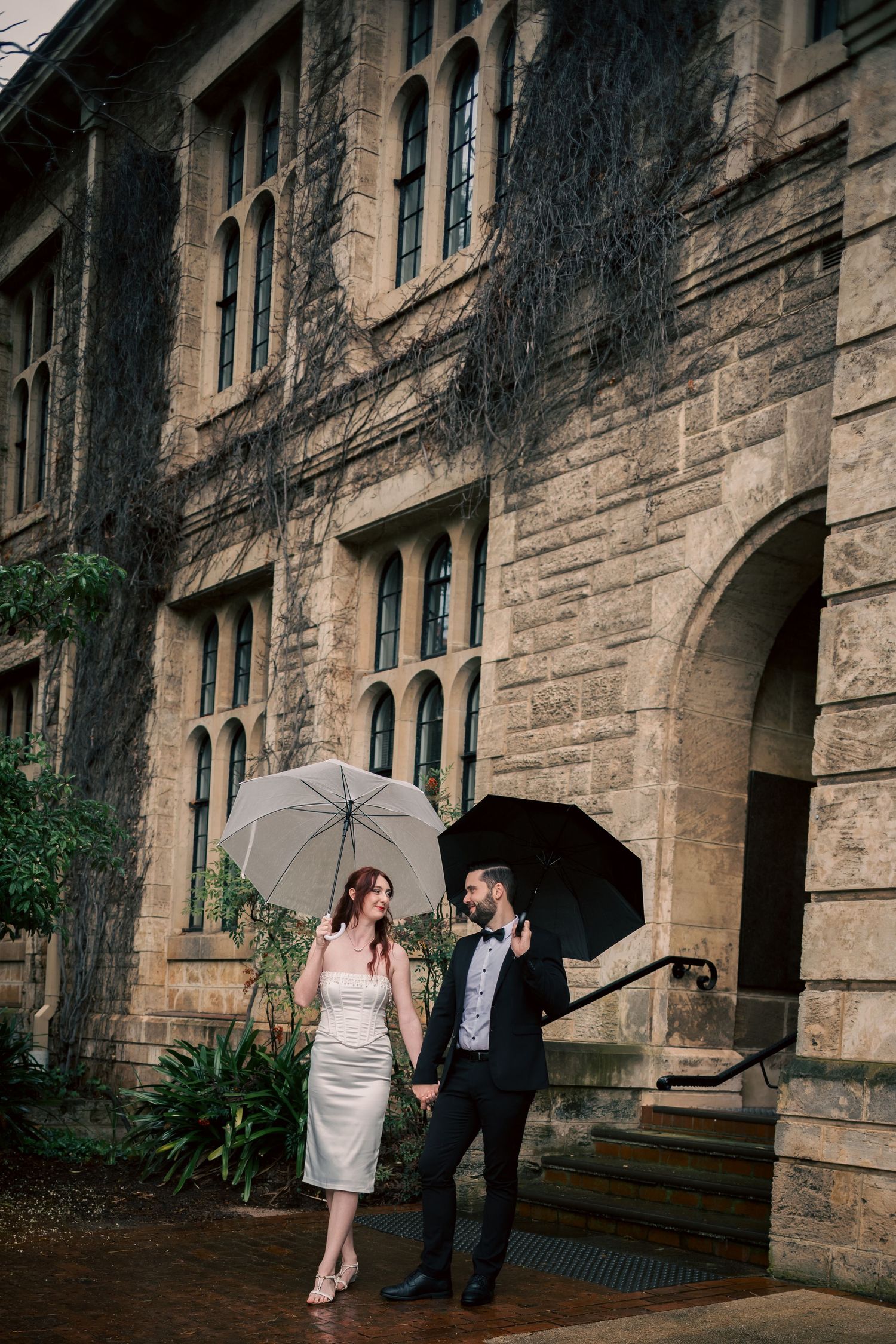 Couple with umbrella poses against historic stone building facade.