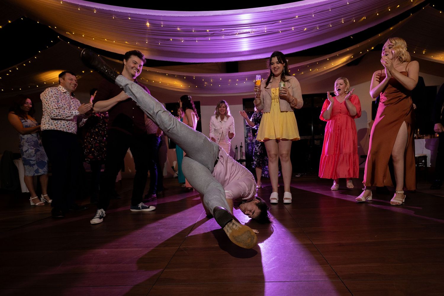 Energetic dance moves on display as wedding guests perform on a purple-lit dance floor during reception.