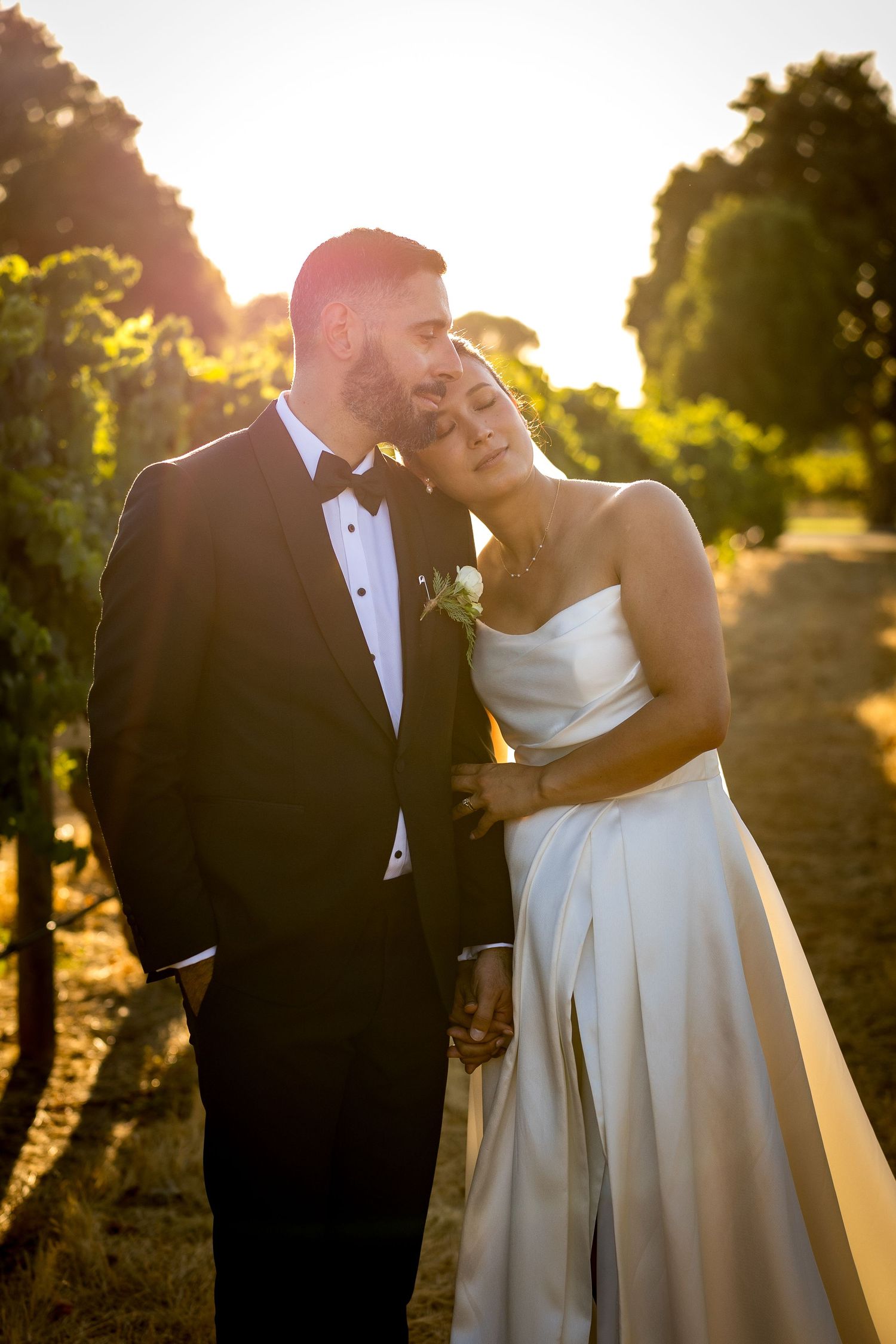 at Mandoon Estate - Bride and groom share a romantic moment in a sun-drenched vineyard, golden hour light glowing behind them.