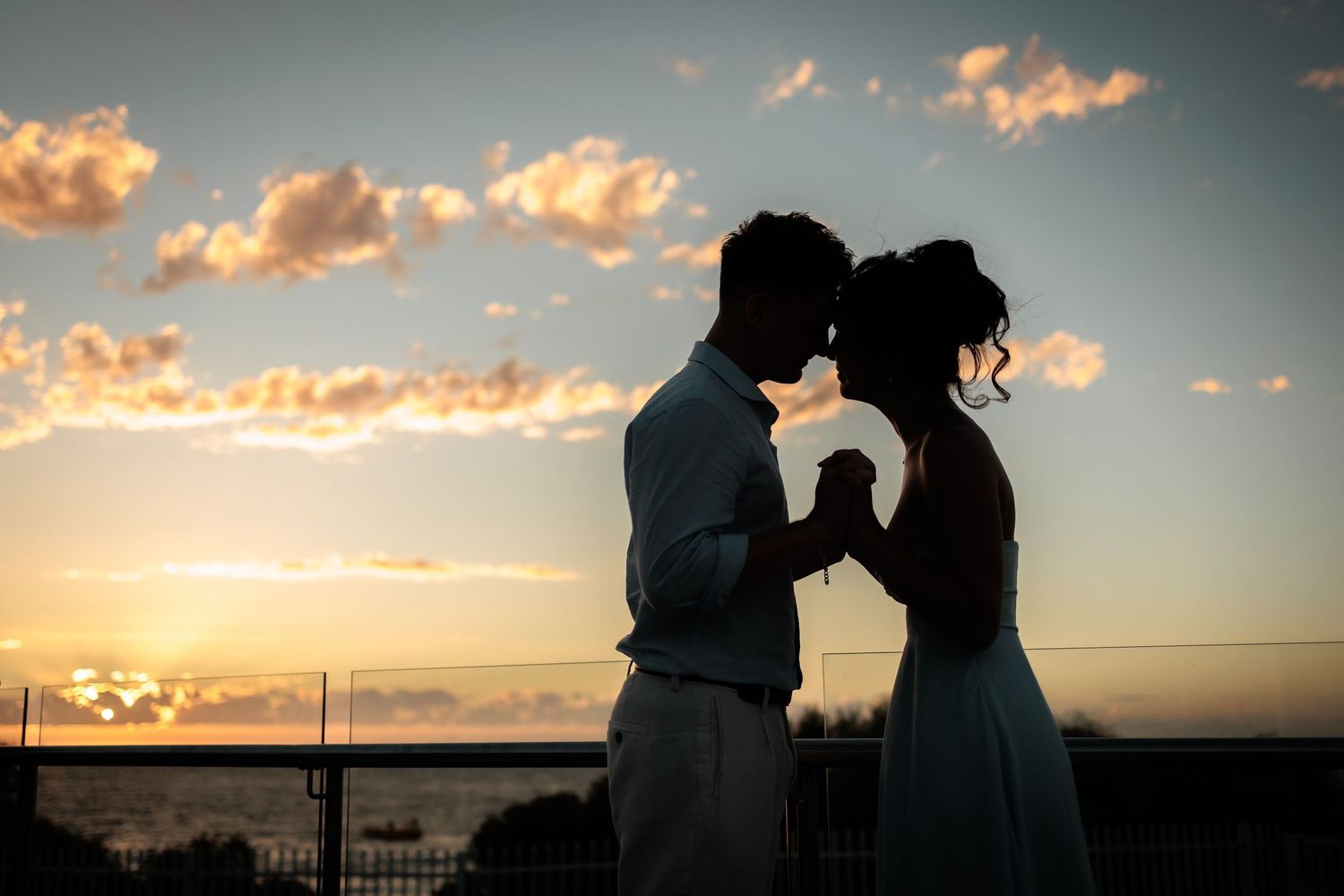 Romantic couple silhouette holding hands at sunset with golden sky and ocean backdrop.