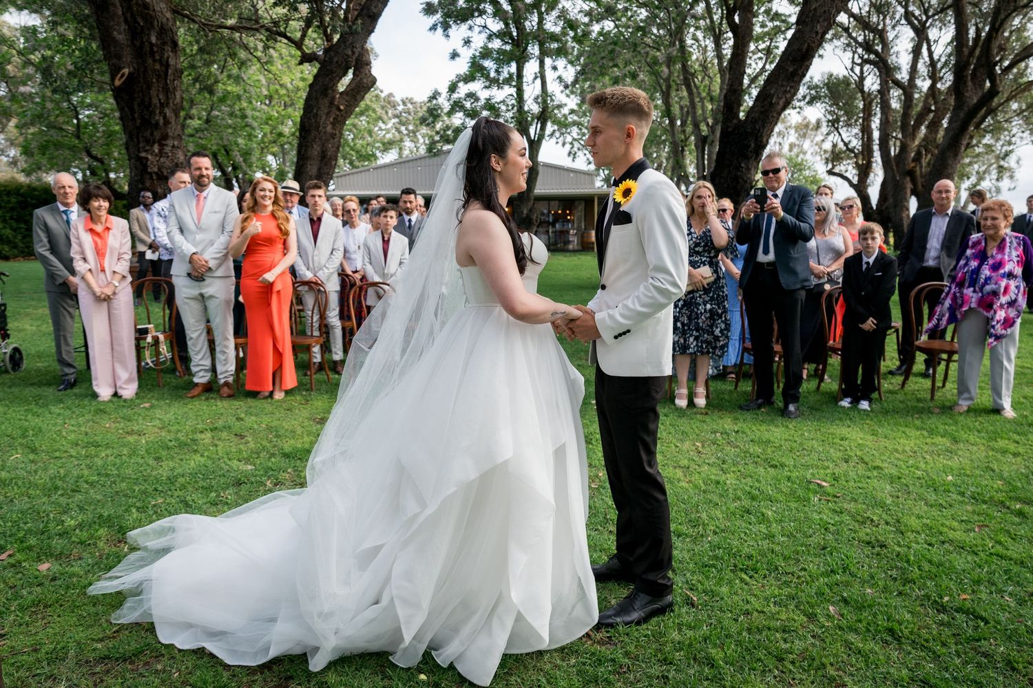 Wedding party and guests gathered on lush green lawn during outdoor celebration.